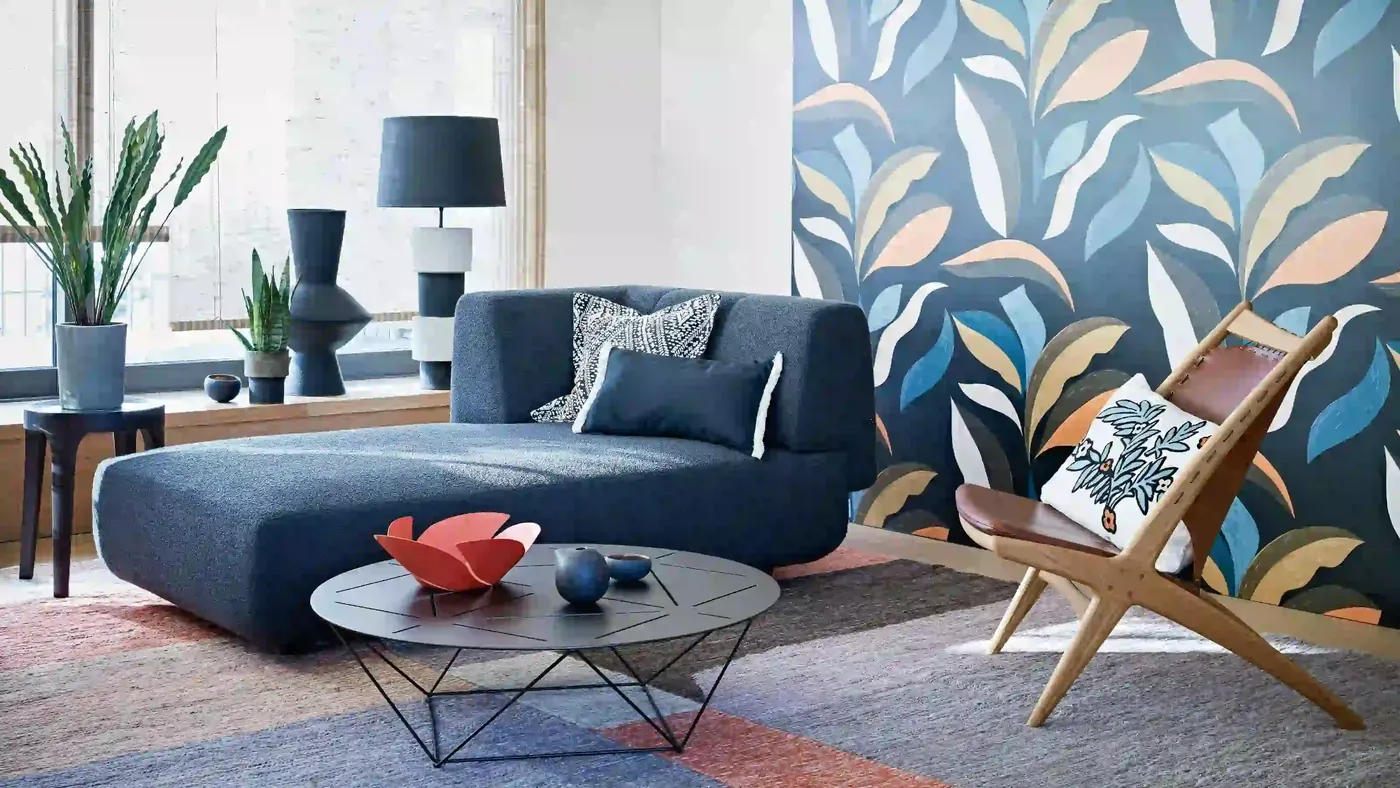 Living room with a large-scale leaf-pattern wallpaper in blue, sand and coral behind a navy sofa